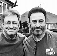 two men standing next to each other in front of a house